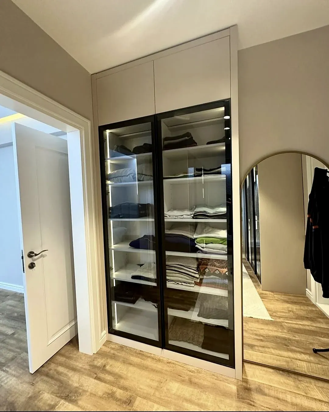 Wardrobe with black-framed glass doors and lit shelves, built by Woodify
