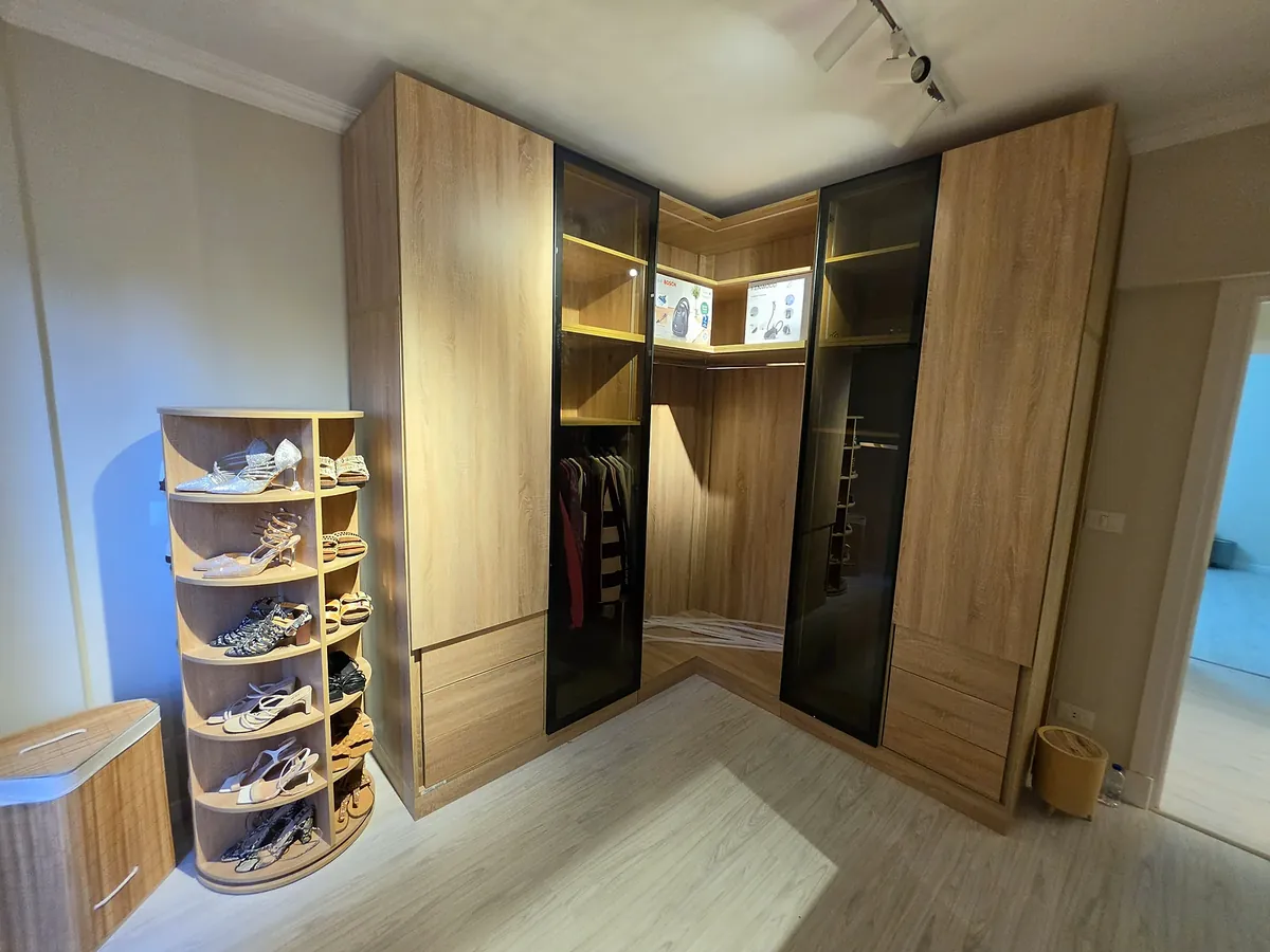 Corner dressing wardrobe in a wood finish with black glass doors and a rotating shoe rack, built by Woodify